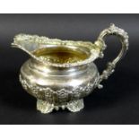 A George IV silver milk jug, with profuse repousse and applied decoration, raised on four shell