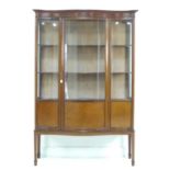 An Edwardian mahogany serpentine fronted display cabinet, line inlaid, bowed glass, three fabric