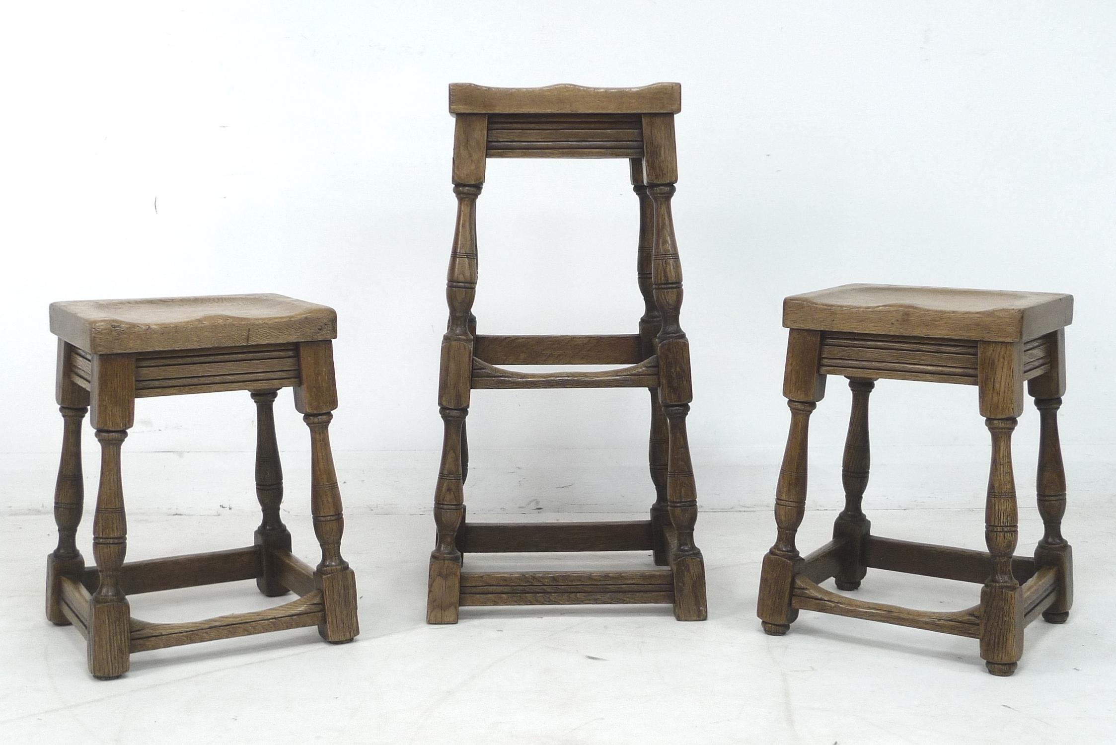 Three 1920s oak stools, comprising a pair, 35 by 40.5 by 77cm high, and taller single stool, 31 by