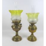 Two Victorian brass paraffin lamps, each with a brass reservoir on circular base, clear glass