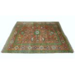 A large Afghan wool rug, with pink/red ground, green borders, and floral decoration overall, 305