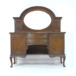 An Edwardian oak sideboard, arched back with inset oval mirror, the base centally with two bow front