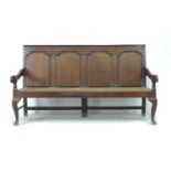 An 18th century oak settle, with four panelled back rest, moulded armrests, resting upon three