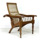 A teak and cane backed reclining planters chair, the arms with spindle support and swivel foot