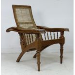 A teak and cane backed reclining planters chair, the arms with spindle support and swivel foot