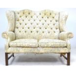 A Georgian style two seater wing back settee, floral embroidered upholstery, raised on channelled