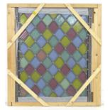 A stained glass window, with yellow, red, blue and green diamond shaped leaded panes, in wooden