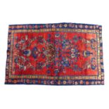 A hand knotted wool Hamadan rug, with zoomorphic designs upon a red ground and with causcasian and
