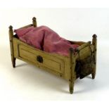 A late 19th century pine doll's bed, painted cream, with turned finials and decorative floral