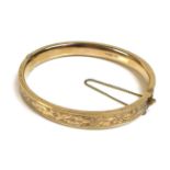 A 9ct gold bangle, with floral bright cut engraved decoration, complete with safety chain, 13.2g