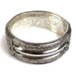 A finely worked broad bangle of Indian style design, the white metal with foliate scrolls, beading