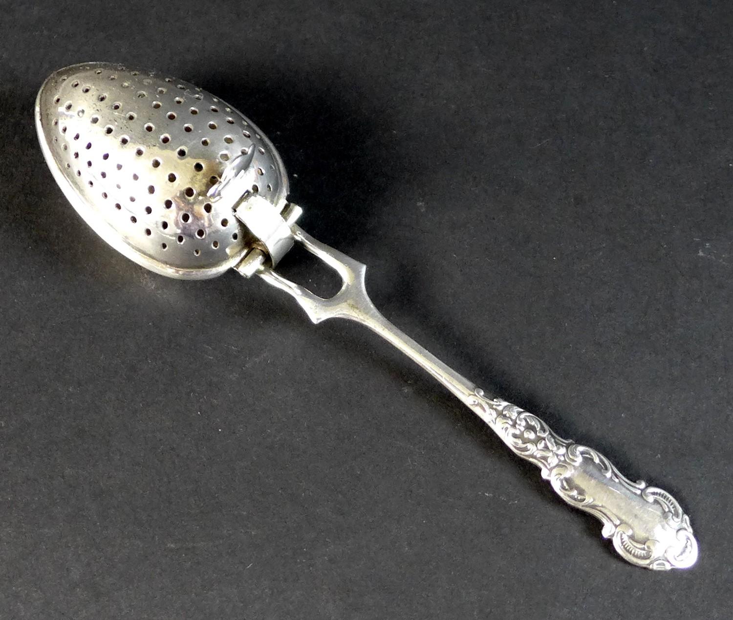 An Edward VII silver tea infuser, fancy scroll decorated handle with two pronged support to the