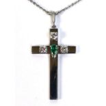 An 18ct white gold cross set with three diamonds and a central pear cut emerald, complete with an