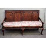 An 18th century oak settle, the panel back above open arms on squat cabriole supports,