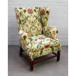 An 18th century wingback armchair, on mahogany block supports, united by stretchers,