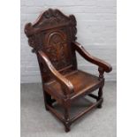 A Charles II style oak wainscot open armchair with carved panel back on baluster turned supports