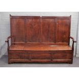 An 18th century oak box seat settle, with a four panel back and open arms, on stile feet,