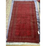 An Afghan rug, the madder field with bands of hexagon medallions bearing flowerheads, a leaf border,
