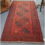 An Afghan rug, the madder field with three and a half bold guls, a zigzag border, 220cm x 114cm.