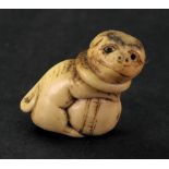 A bone netsuke, carved in the form of a dog wearing a collar and clasping a ball, 4cm high.