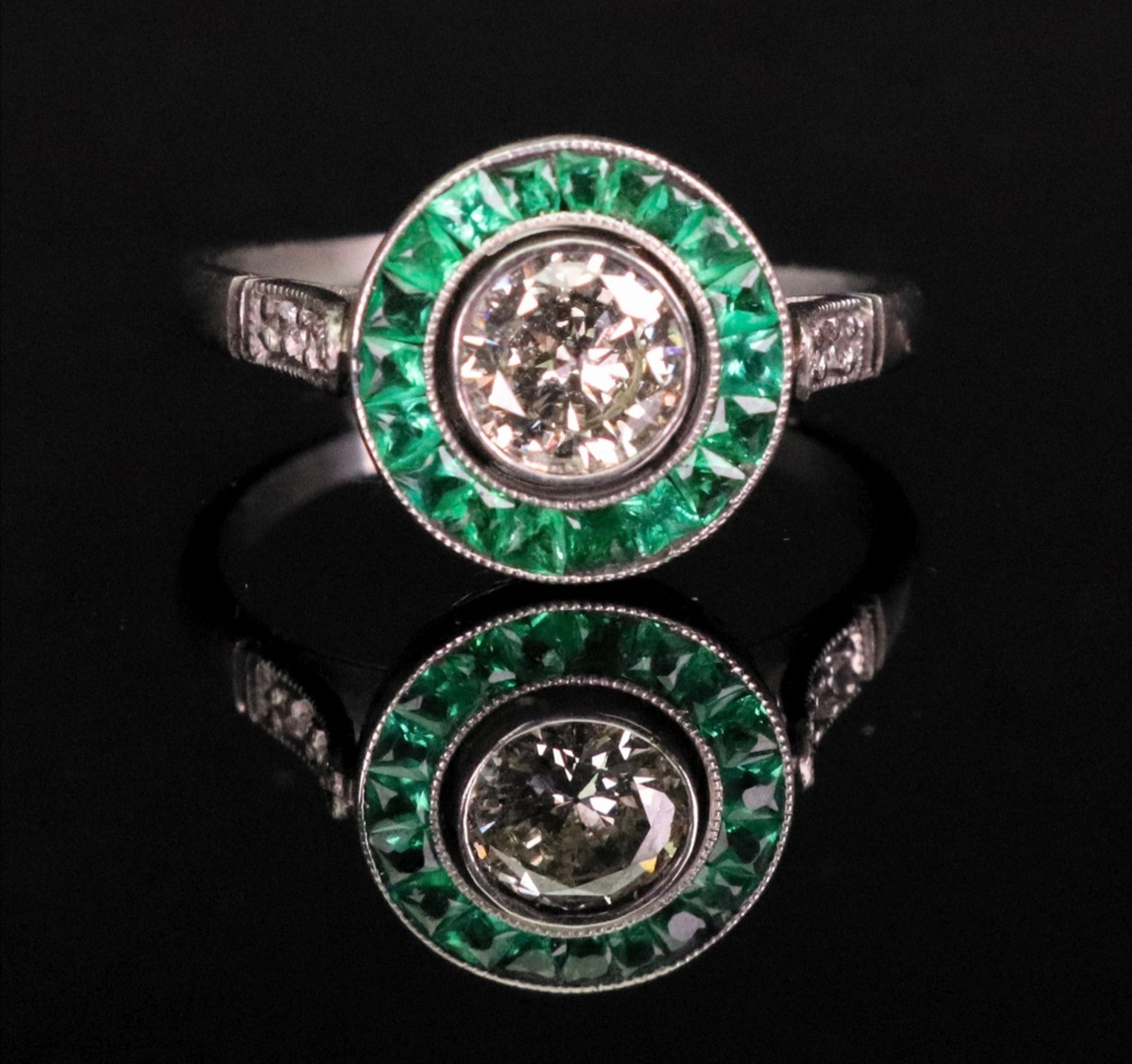 An emerald and diamond ring of circular cluster design,