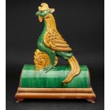 A Chinese pottery sancai glazed roof tile, in the form of a phoenix, mounted on a hardwood stand,