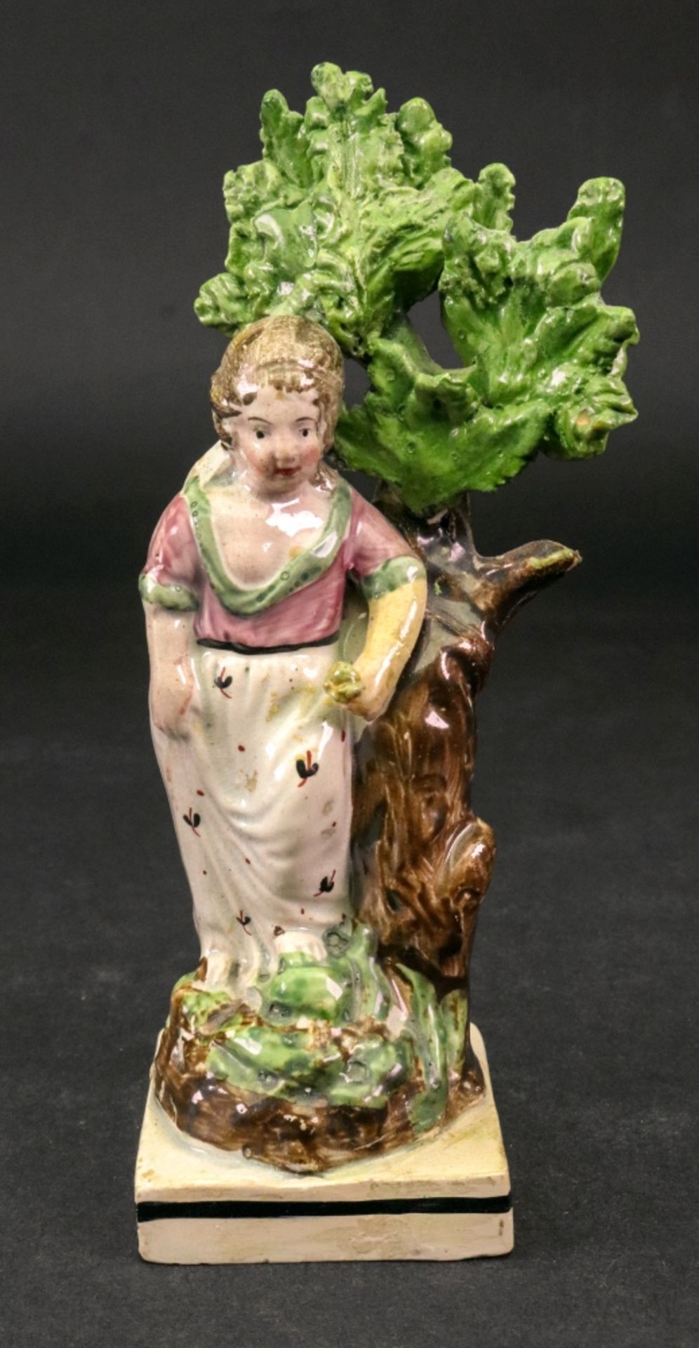 A Staffordshire pearlware figure of a girl, circa 1800, modelled standing against a tree,