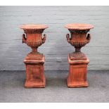 A pair of terracotta urns, with egg and dart rims and twin handles, on stepped square bases,