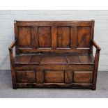 An 18th century oak box seat settle, the four panel back over open arms and lift seat on block feet,