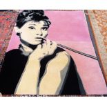 A machine made rug, the pink field depicting Audrey Hepburn, smoking a cigarette in a long holder,