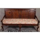 An 18th century oak settle, the panel back above open arms on squat cabriole supports,