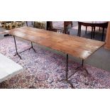 A pine kitchen table, the triple plank top on a pair of wrought iron trestle supports,