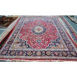 A Mashhed carpet, Persian, a madder field with a bold medallion and matching sprandrels,