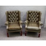 A pair of George II style brass studded green leather upholstered wingback armchairs on block