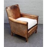 An early 20th century studded brown leather upholstered easy armchair on tapering block supports,