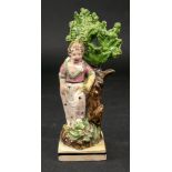 A Staffordshire pearlware figure of a girl, circa 1800, modelled standing against a tree,