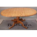 A 20th century pine circular extending dining table on baluster column and four downswept supports,