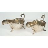 A pair of silver sauceboats, each with a shaped rim, scrolling handle and raised on three feet,
