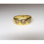 A gold and diamond set three stone ring, star gypsy set with a row of cushion shaped diamonds,