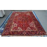 A Heriz carpet, Persian, the madder field with a bold dark indigo medallion, ivory spandrels,