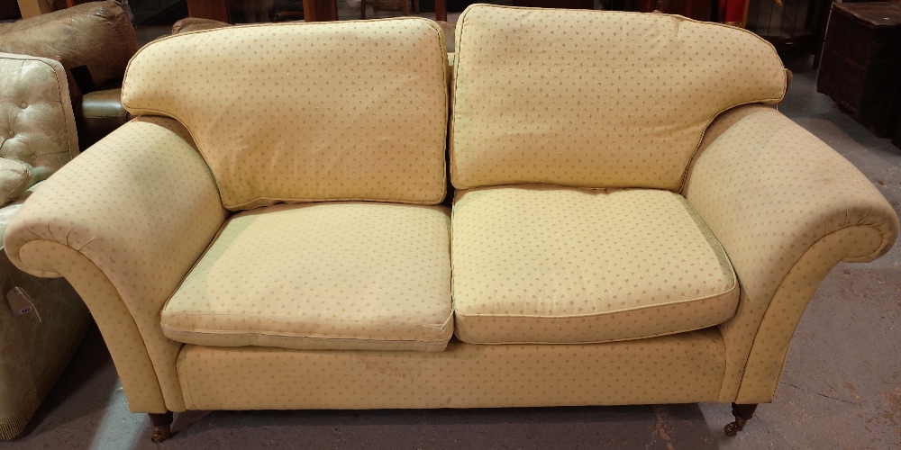 A 20th century hardwood framed two seater sofa with roll over arms on turned supports,