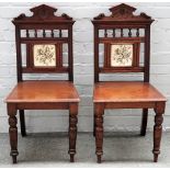 A pair of Victorian walnut framed hall chairs with tile inset backs and turned supports,