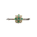 An emerald and diamond set bar brooch, of flowerhead design, claw set with step-cut,