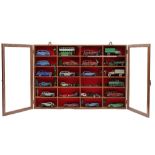 Twenty-four pre-war Dinky die-cast vehicles and related items in a glazed mahogany wall cabinet,