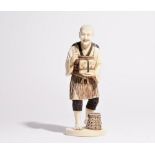 A Japanese ivory okimono of a man, carved standing holding a box, a basket at his feet, 21cm high.