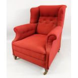 An Edwardian wing back armchair, in George III style, button down upholstered in red material,