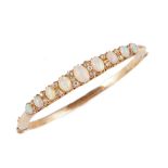 A gold, opal and diamond set oval hinged bangle, mounted with a row of nine graduated oval opals,