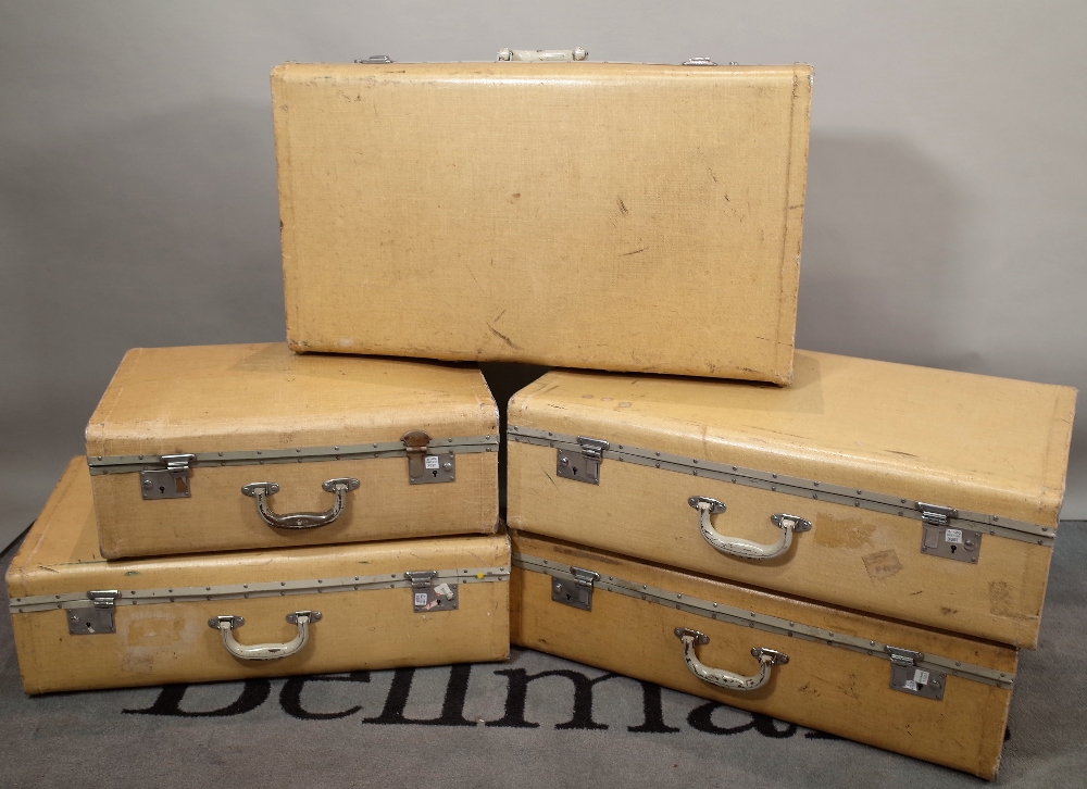 A group of five cream canvas suitcases, the largest 76cm wide x 22cm high.
