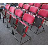 A bank of four red upholstered folding theatre seats, on black metal tubular frames,