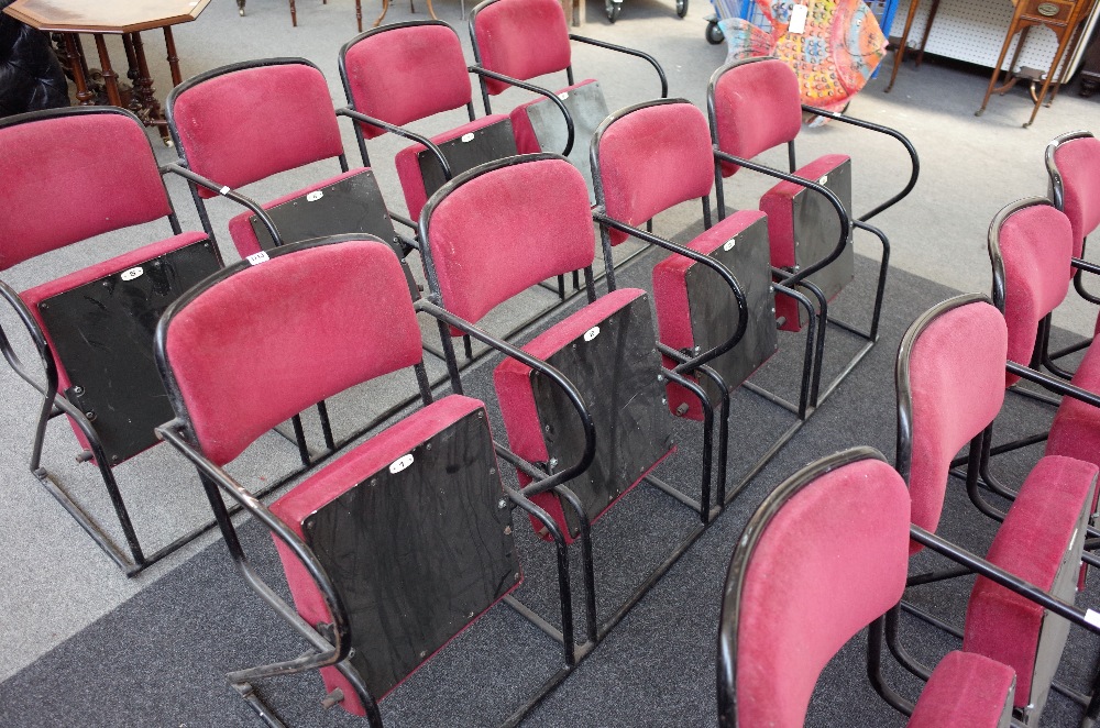 A bank of four red upholstered folding theatre seats, on black metal tubular frames,